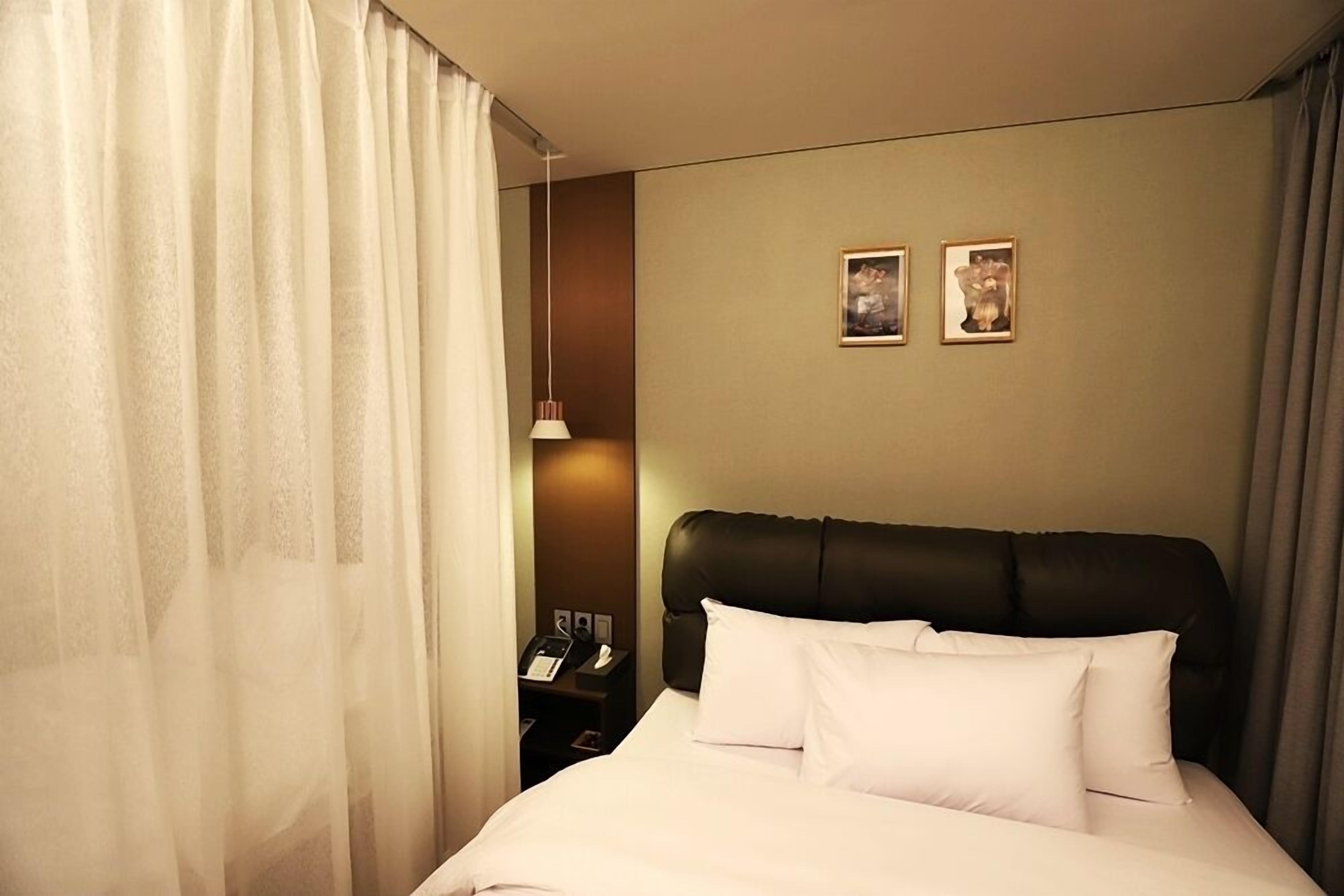 A hotel room with a bed, a nightstand with a phone, and two framed pictures on the wall.