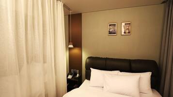 A hotel room with a bed, a nightstand with a phone, and two framed pictures on the wall.