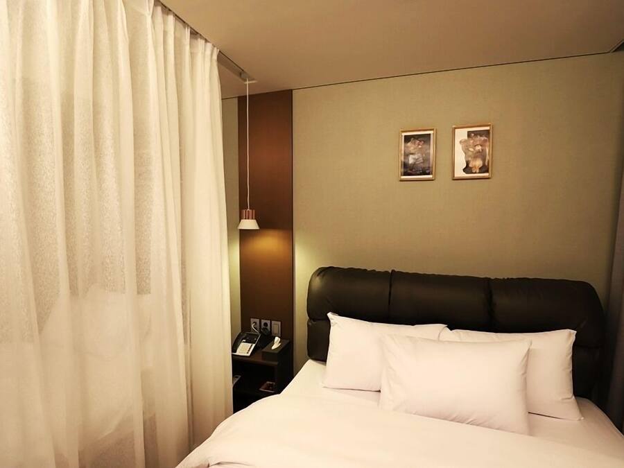 A hotel room with a bed, a nightstand with a phone, and two framed pictures on the wall.