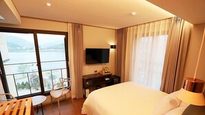 A hotel room with a large bed, a TV mounted on the wall, a desk with a chair, and a view of a body of water through large windows. - Namyangju Bukhangang Dolce Casa Hotel (Namyangju)