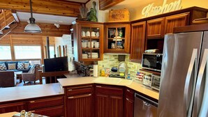 A kitchen with wooden cabinets, a stainless steel refrigerator, a microwave, and a dishwasher. - Spectacular 3-Story 7BR CDA Lakefront w-Dock on Secluded Powderhorn Bay (Harrison)