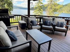 Een terras met buitenmeubilair, een barbecue en uitzicht op een meer en bos.