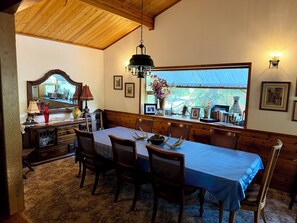Un comedor con una mesa larga, sillas, una araña, un espejo y una ventana con vistas.