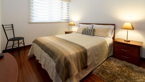 A bedroom with a bed, two bedside tables with lamps, a chair, and a window with blinds. - Spacious, modern, GREAT LOCATION netflix, wifi, cable, 2BEDROOM, 2BATHROOM (La Carolina)