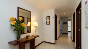 A hallway with a wooden console table, a mirror, a vase with flowers, a standing lamp, and a rug. - Spacious, modern, GREAT LOCATION netflix, wifi, cable, 2BEDROOM, 2BATHROOM (La Carolina)