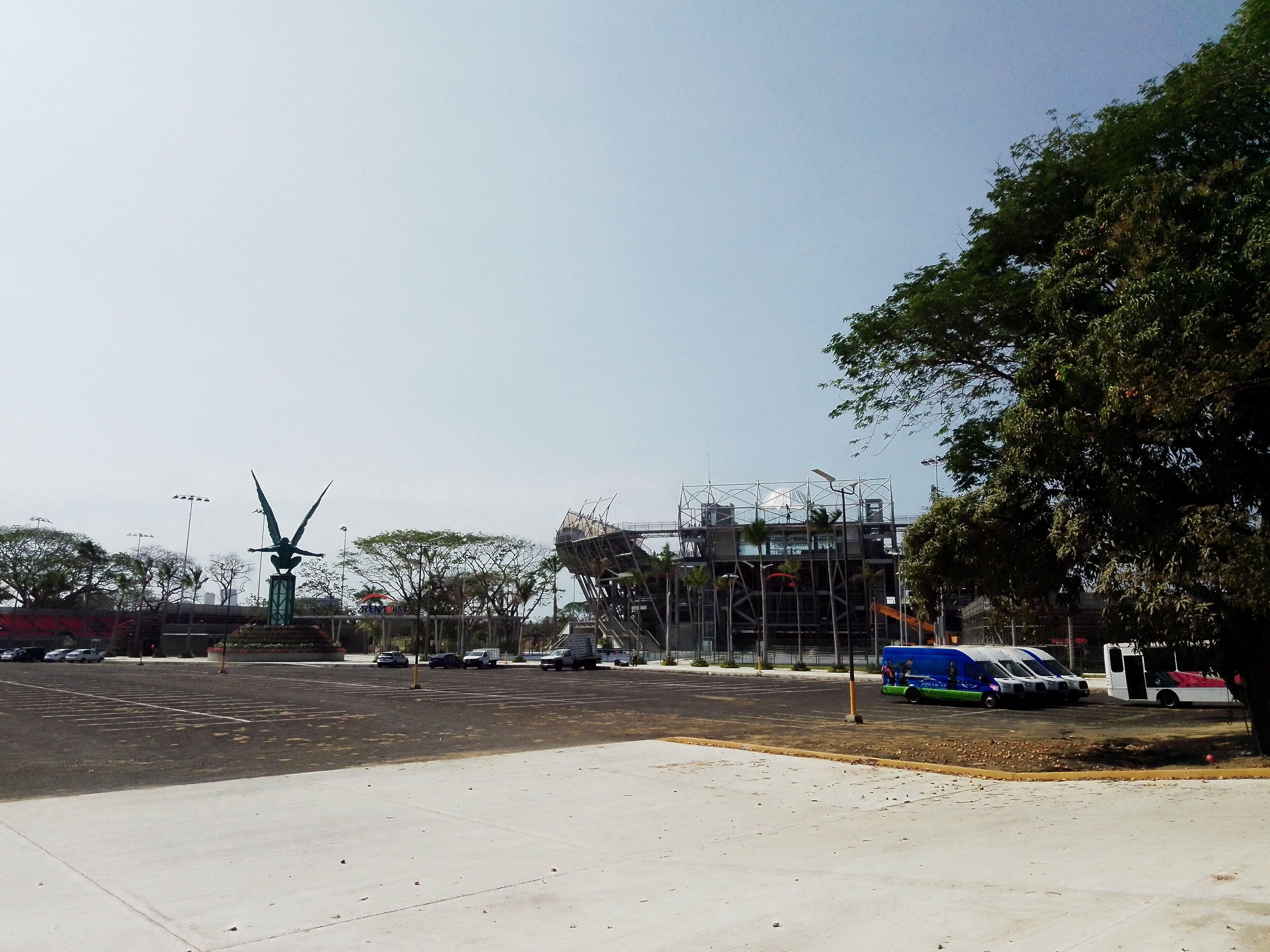A parking lot with a few cars, a large sculpture, and a building under construction.