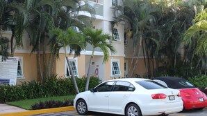 A white car parked in a lot with palm trees and a building in the background. - Nice Apartment, perfect for families!  (Diamante Lakes)