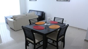 A dining table with four chairs, a white sofa, and a black leather chair in a room with white walls and tiled flooring. - Nice Apartment, perfect for families!  (Diamante Lakes)