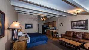 A hotel room with a bed, a desk, a coffee table, a sofa, a kitchenette, and a ceiling fan. - Windjammer Lodge (Ogdensburg)