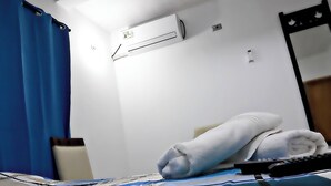 Een hotelkamer met een bed, een blauw gordijn, een airconditioning, een spiegel en een handdoek op het bed.