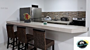Een moderne keuken met een roestvrijstalen koelkast, een inbouwoven, een broodrooster en een spoelbak. Er staan drie rieten stoelen bij het aanrecht.