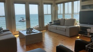 A spacious living room with a large window overlooking the sea, a sofa, a coffee table, and a television. - Living on the edge! Breathtaking waterfront living at it’s best!  (Provincetown)