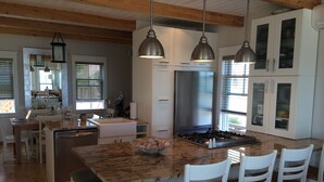 A modern kitchen with white cabinets, a stainless steel refrigerator, and a marble island with bar stools. - Living on the edge! Breathtaking waterfront living at it’s best!  (Provincetown)