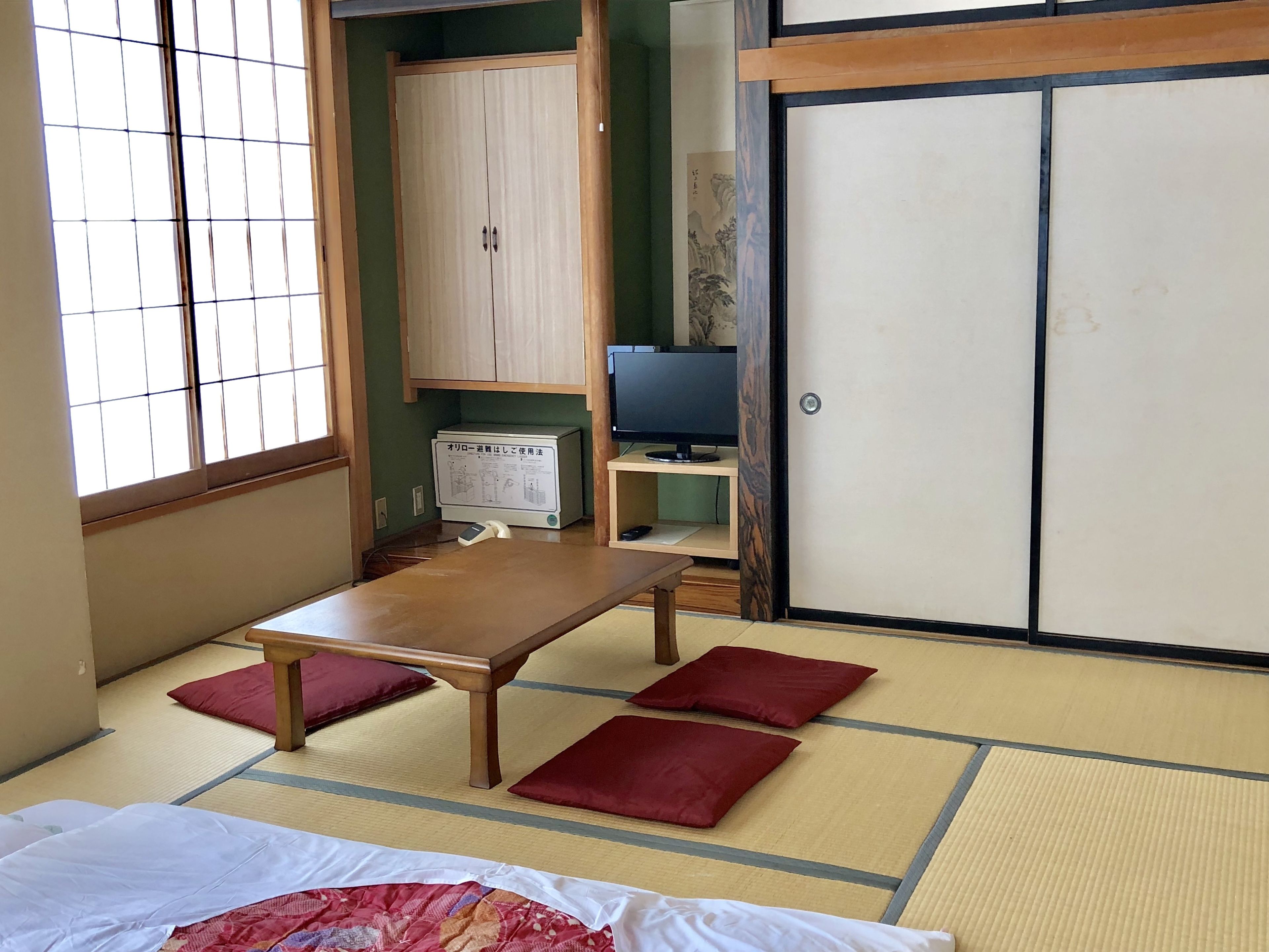 A traditional Japanese room with tatami flooring, a futon bed, a low wooden table, and a television.