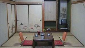 A traditional Japanese room with tatami flooring, a low table with cushions, sliding doors with artwork, and a small TV. - Resort Inn Fujihashi (Fujikawaguchiko)