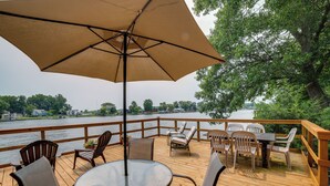 Una terraza con mesa y sillas, un paraguas grande y vistas al río.
