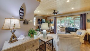 Una sala de estar acogedora con techo de madera, un sofá, una mesa con lámparas y un televisor.