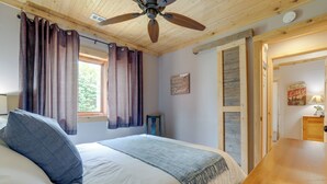 Un dormitorio con cama, ventilador de techo, ventana con cortinas, una puerta y un cartel en la pared.