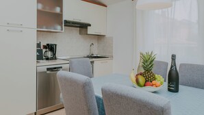 A modern kitchen with white cabinets, a dishwasher, and a dining area with a table set for two. - Villa DANEX STANDARD **** (Umag)