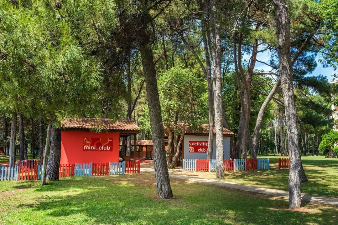 A red and white building labeled 'mini club' surrounded by trees and a colorful fence.