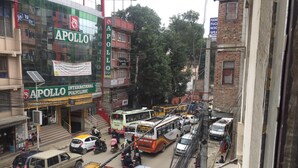 A busy street with various vehicles, including buses and cars, and a building with a sign for 'APOLLO INTERNATIONAL POLYCLINIC'. - Home aboard with the same feeling of home in Nepal  (Kathmandu)