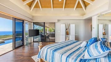 A bedroom with a large bed, a television, and a view of the ocean.