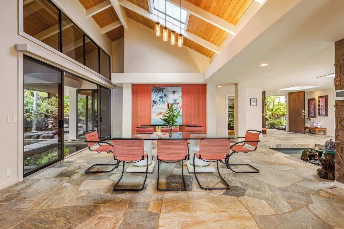 Un vaste espace dédié à la salle à manger, avec une table et des chaises en verre, un plafond en bois et une vue sur l’extérieur.