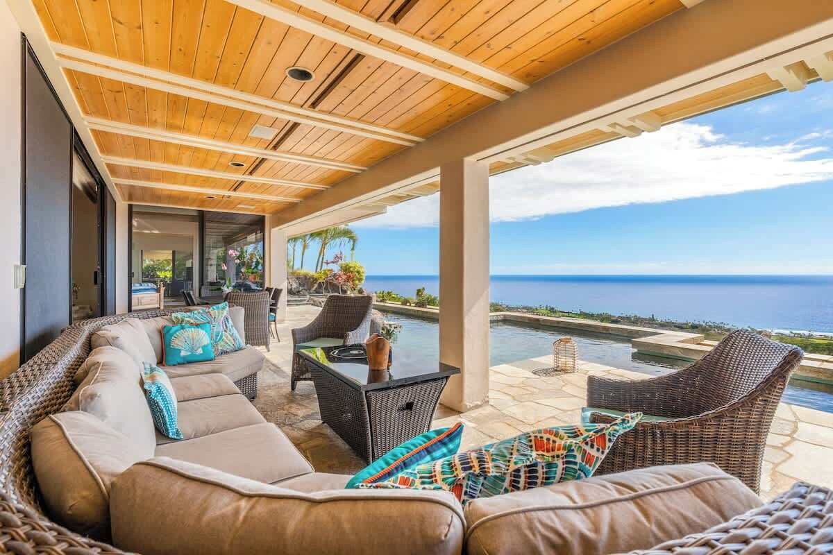 Uma área de estar coberta ao ar livre com vista para o oceano, com um sofá, cadeiras e uma mesa.