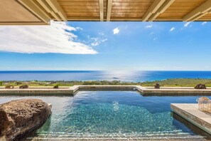 A clear view of a swimming pool with a view of the ocean, surrounded by rocks and a wooden ceiling structure. - Watch Rain Fall Inside Your Home Into The Indoor W (Kailua-Kona)