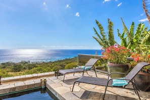 A balcony with two lounge chairs, a pool, and a view of the ocean.