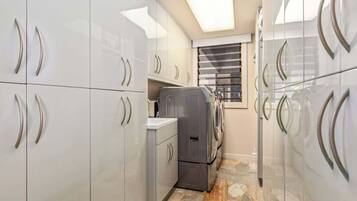 A compact kitchen with white cabinets, a built-in washer and dryer, and a window with blinds.