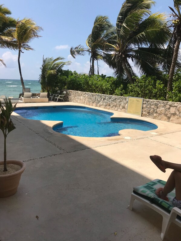 A swimming pool with a stone wall, lounge chairs, and a view of the ocean.