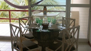 A dining area with a glass table and white chairs, overlooking a palm tree and ocean view.