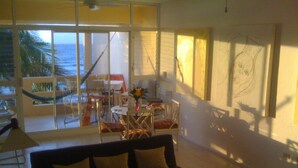 A living room with a large window overlooking a balcony, a sofa, a coffee table, and a dining area with chairs and a table.