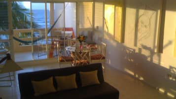 A living room with a large window overlooking a balcony, a sofa, a coffee table, and a dining area with chairs and a table.