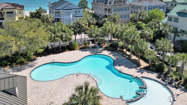 A resort with a large, curved swimming pool surrounded by palm trees and beachfront views. - Cordy Beach House - 2nd Row Ocean View, Gated with Pool! (Pawleys Island)