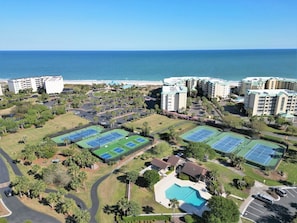 Un resort con diversi campi da tennis, piscina e vista sul mare.