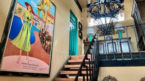 Uma escadaria com um candelabro, um cartaz emoldurado e uma porta verde-água.