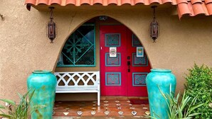 Entrada de um edifício com uma porta vermelha, um banco branco e dois grandes vasos turquesa.