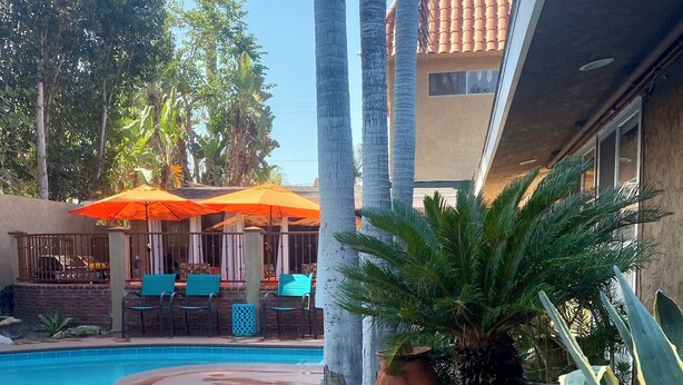 Uma piscina com área de estar, palmeiras e um edifício com telhado em azulejos.