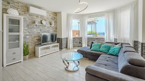 A modern living room with a stone wall, a grey sofa, a glass coffee table, and a TV on a white stand. - ..it's your place!... (Los Cristianos)