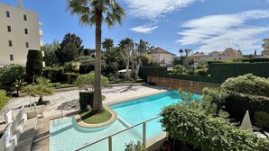 Une piscine entourée de verdure, avec un palmier et une haie au premier plan.