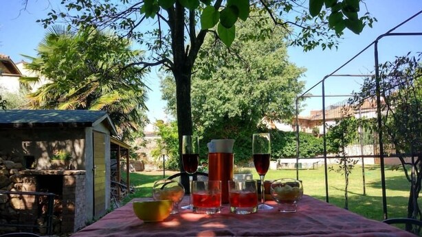 An outdoor dining area with a table set for two, featuring a red tablecloth and various dishes and drinks.