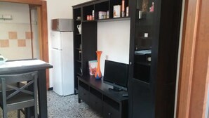 A compact living space with a kitchenette, a TV on a stand, and a small table.