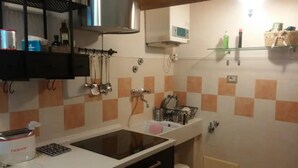 A kitchen with a sink, stove, and various utensils. There is a shelf above the sink with bottles and a small mirror.