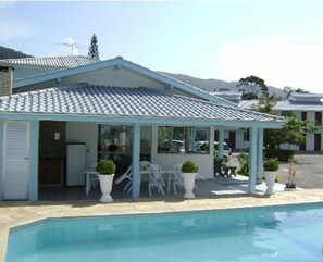 A building with a covered patio area, a pool, and a mountainous backdrop. - Pousada Talismã (Florianópolis)