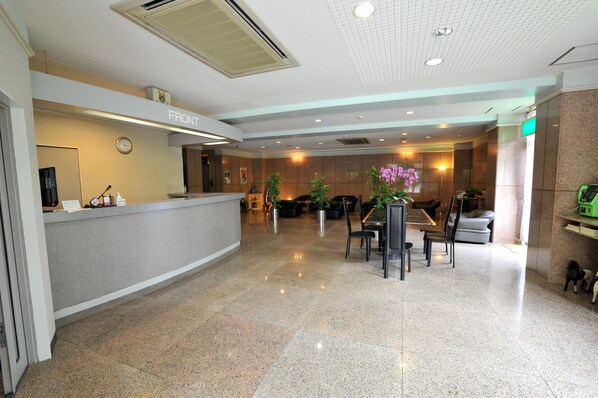 A hotel reception area with a reception desk, seating area, and a clock on the wall. - Hotel Yamadasou (Nago)