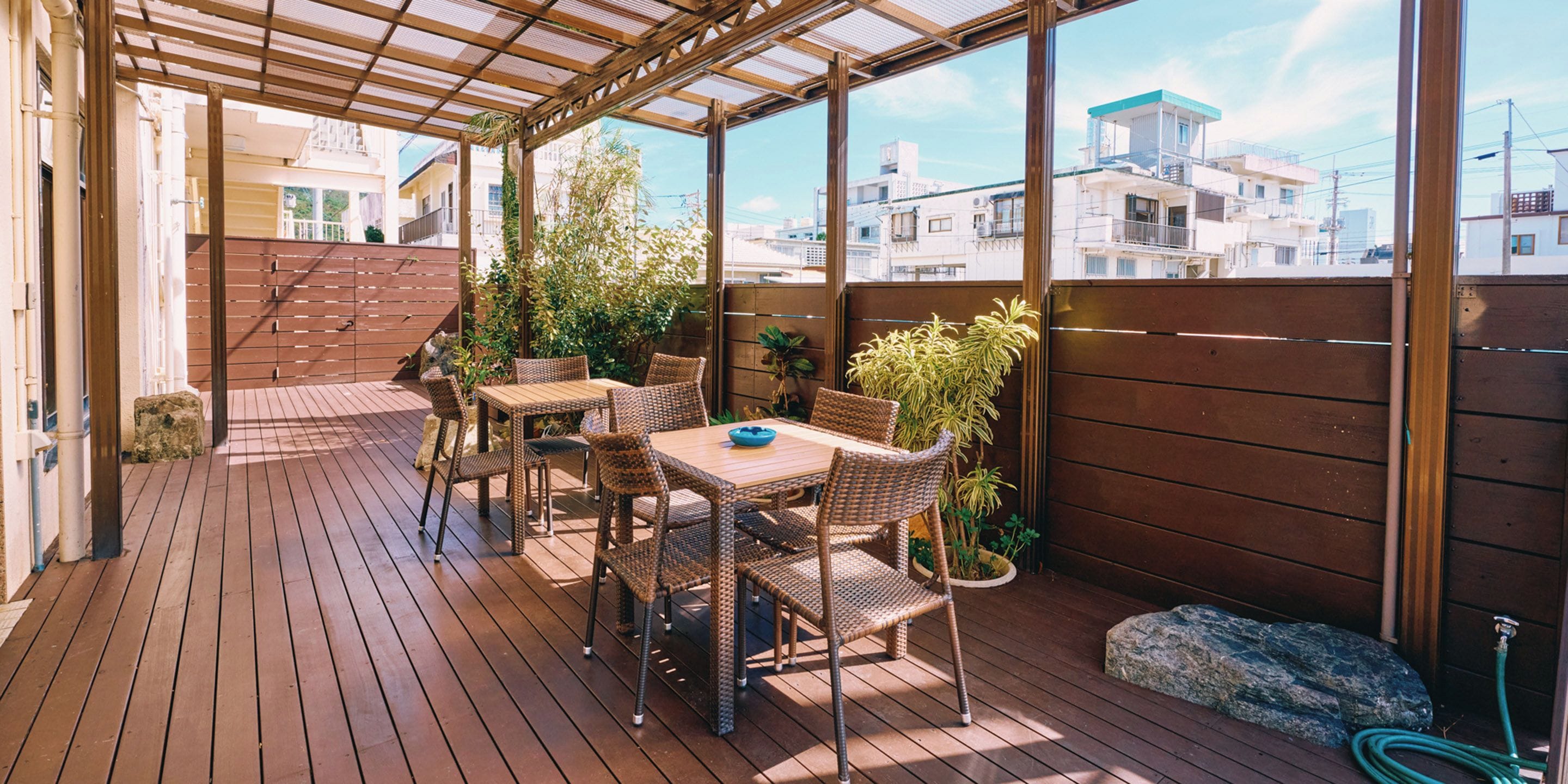 An outdoor patio with wooden flooring, wicker furniture, and potted plants.