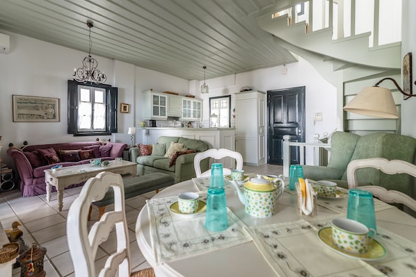 A cozy living room with a dining table set for tea, a sofa, and a kitchen in the background. - Villa SEAlia Elegantseasidein Spetses (Spetses)