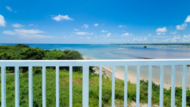 A coastal view from a balcony with a railing, clear blue sky, and a sandy beach.